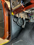 A black speaker enclosure installed in the kick panel area of a vehicle, with visible wiring and part of the car's interior.
